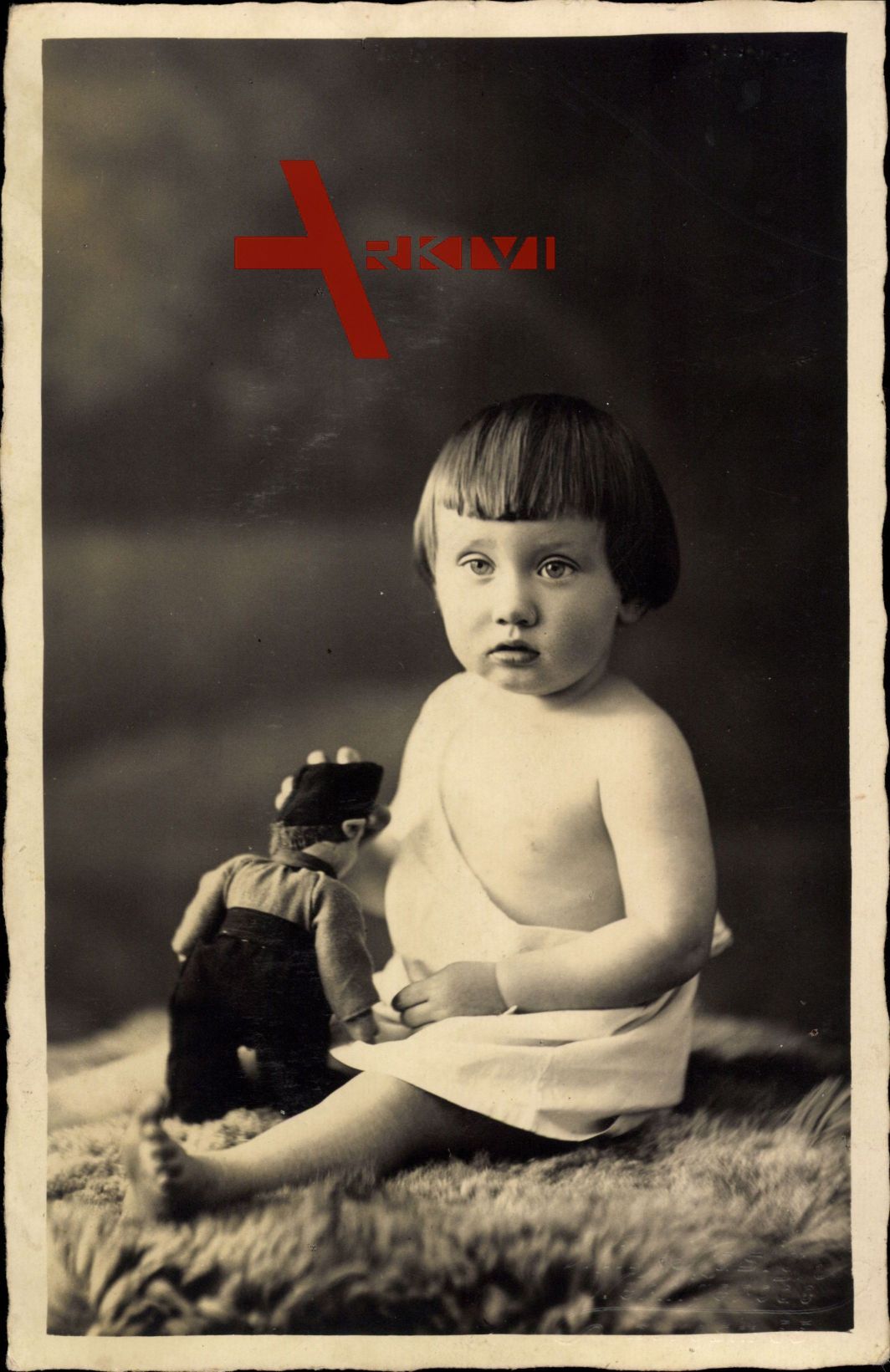 Kleinkind mit Puppe sitzt auf einem Tierfell, Spielzeug